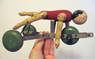 Side view of wooden swimming toy depicting a man who moves his legs and arms as the toy is rolled on its wheels in pretend water.